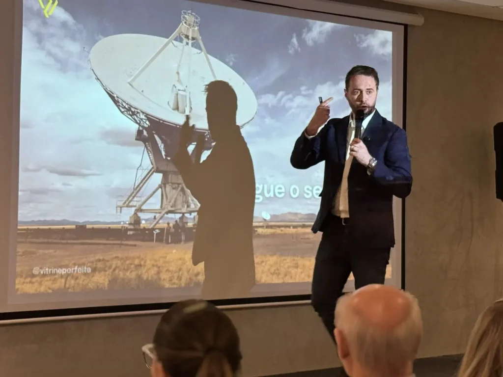 Francisco Issler fala ao microfone ao lado do telão durante a palestra Tudo é Vitrine no Sindilojas Fronteira Noroeste, em Santa Rosa (RS)